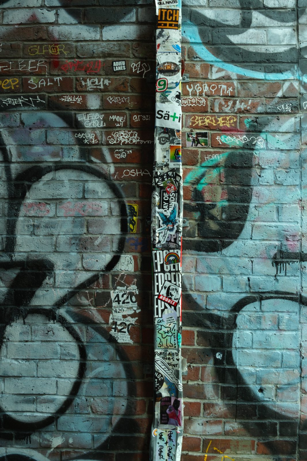 A rainpipe running down the side of a brick building covered in graffiti and stickers.
