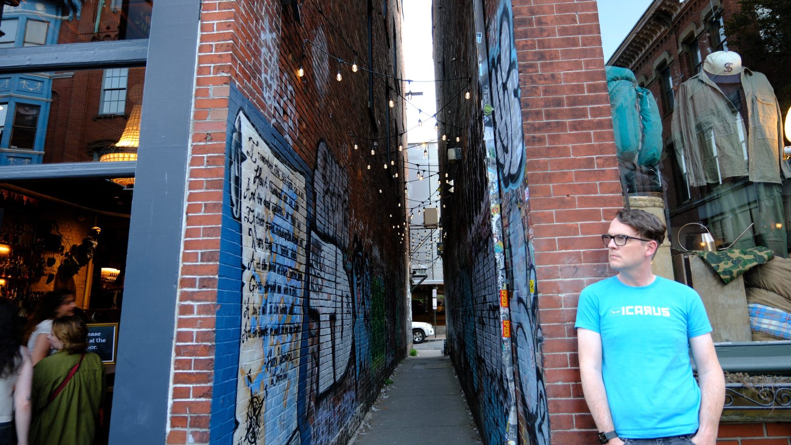Blue shirt man standing by alley while people enter a restaurant