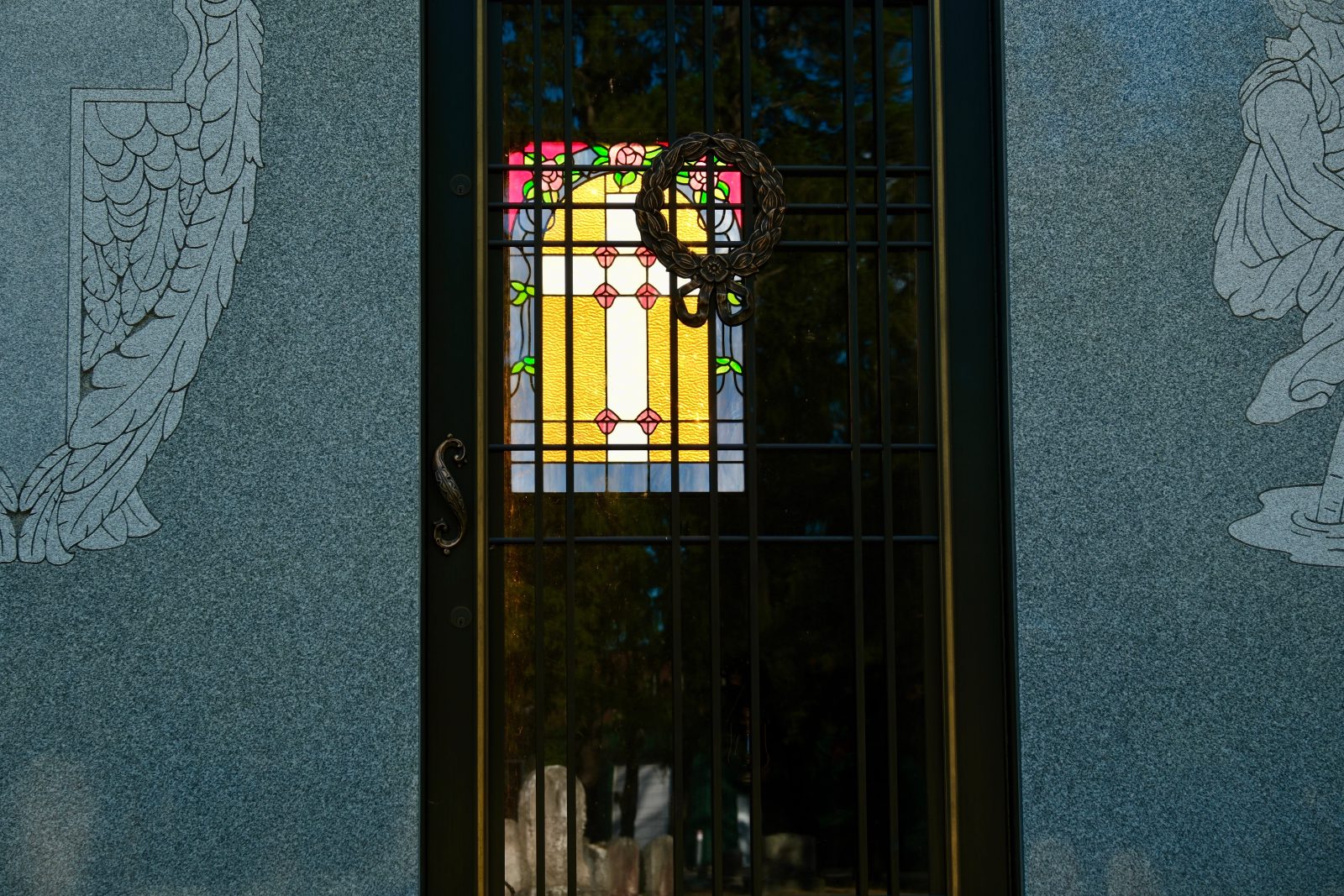 Closeup of the details of a Mausoleum looking through the gated front door to a stained glass window on the back