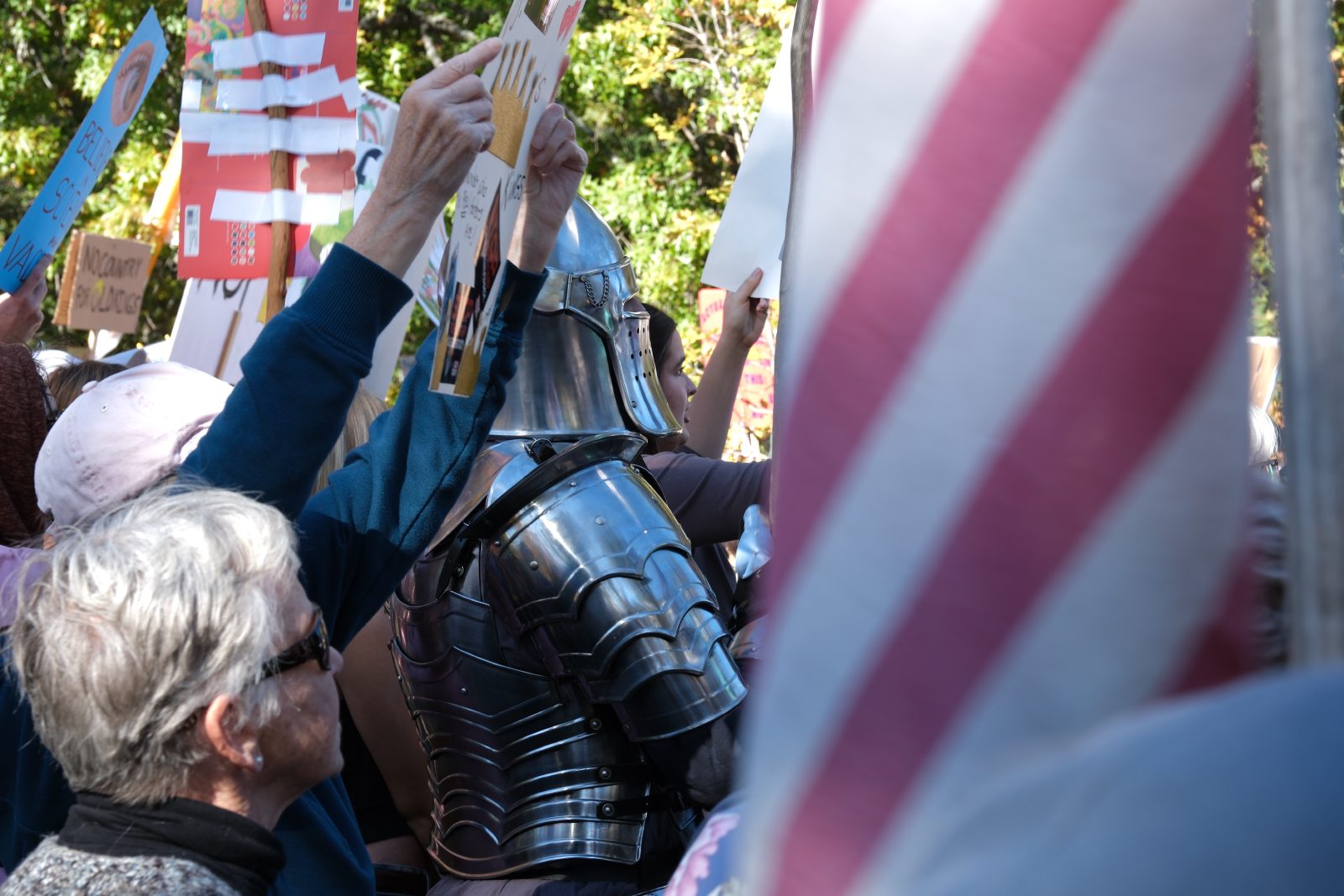 A person in a full middle ages suit of armor in a large protest crowd