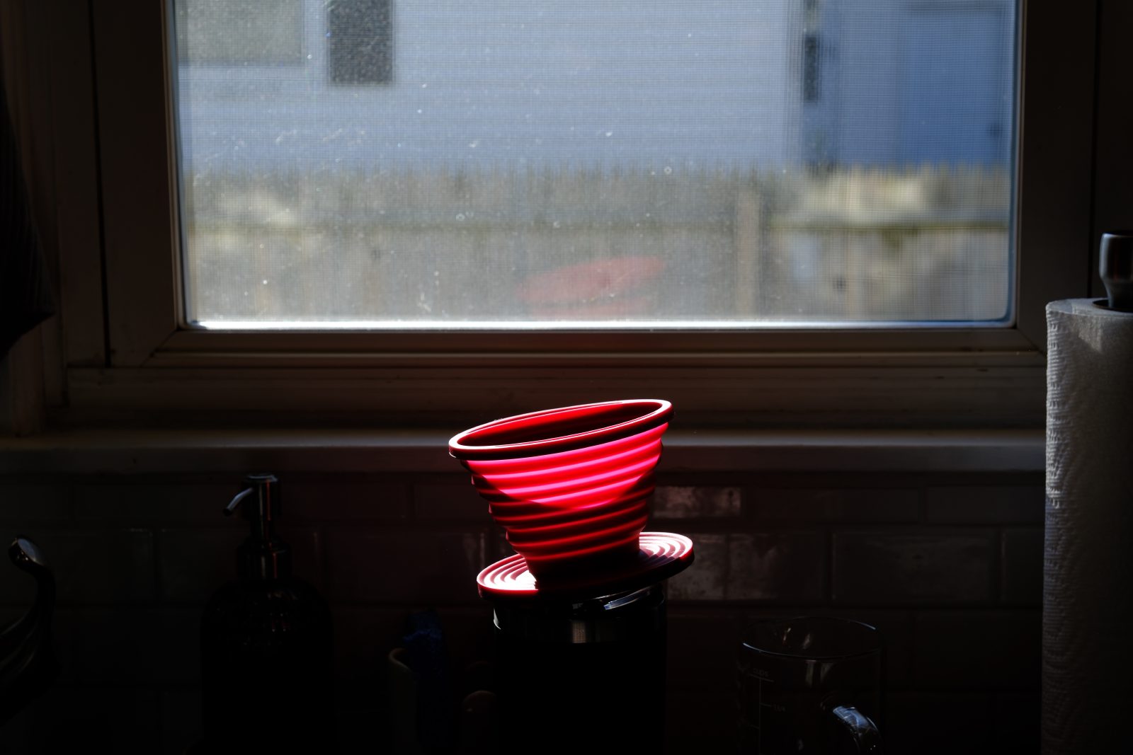 Red, silicone pour through sitting on coffee mug by sink
