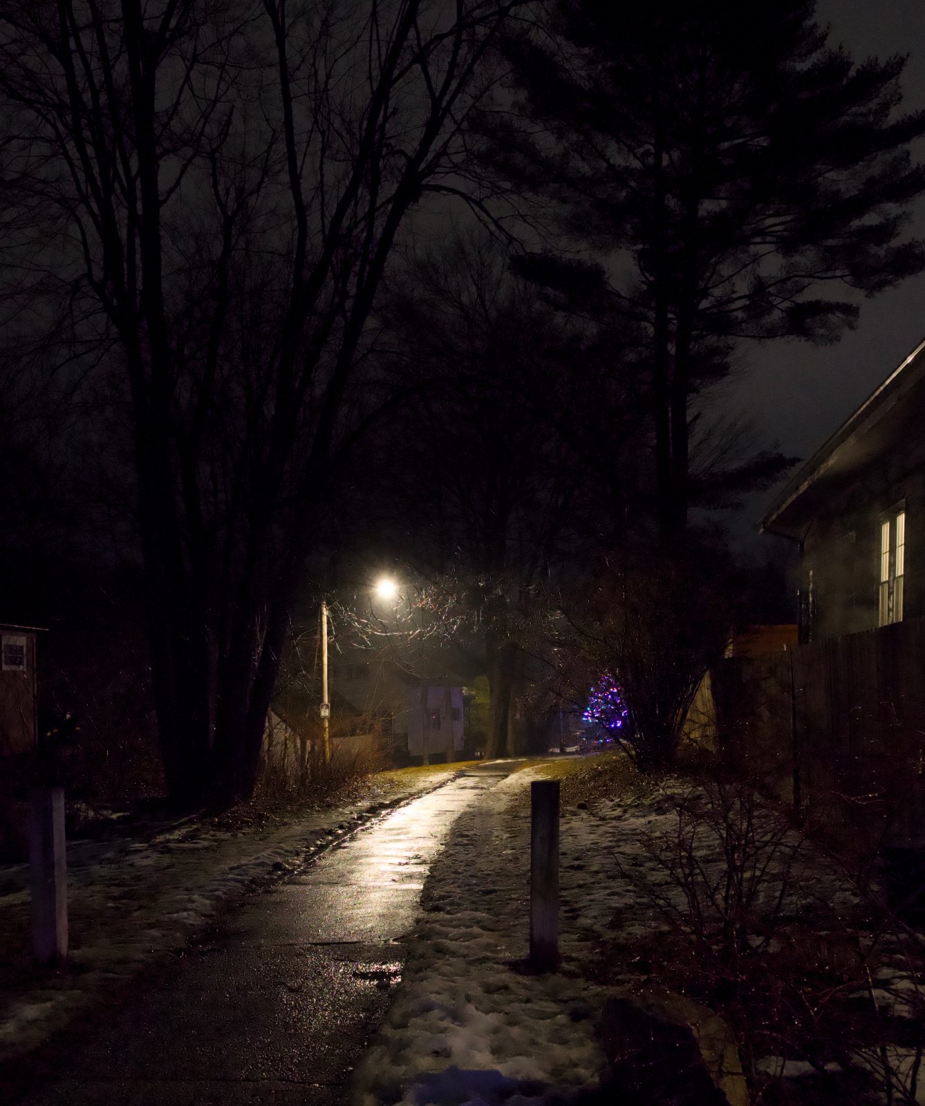 A paved path lit by a single streetlamp on a rainy night.