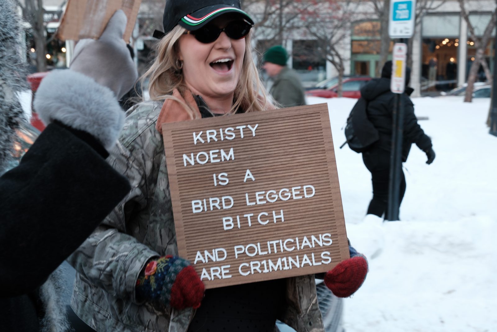 A protest sign reading, 'Kristy Noem is a bird legged bitch and politicians are criminals'