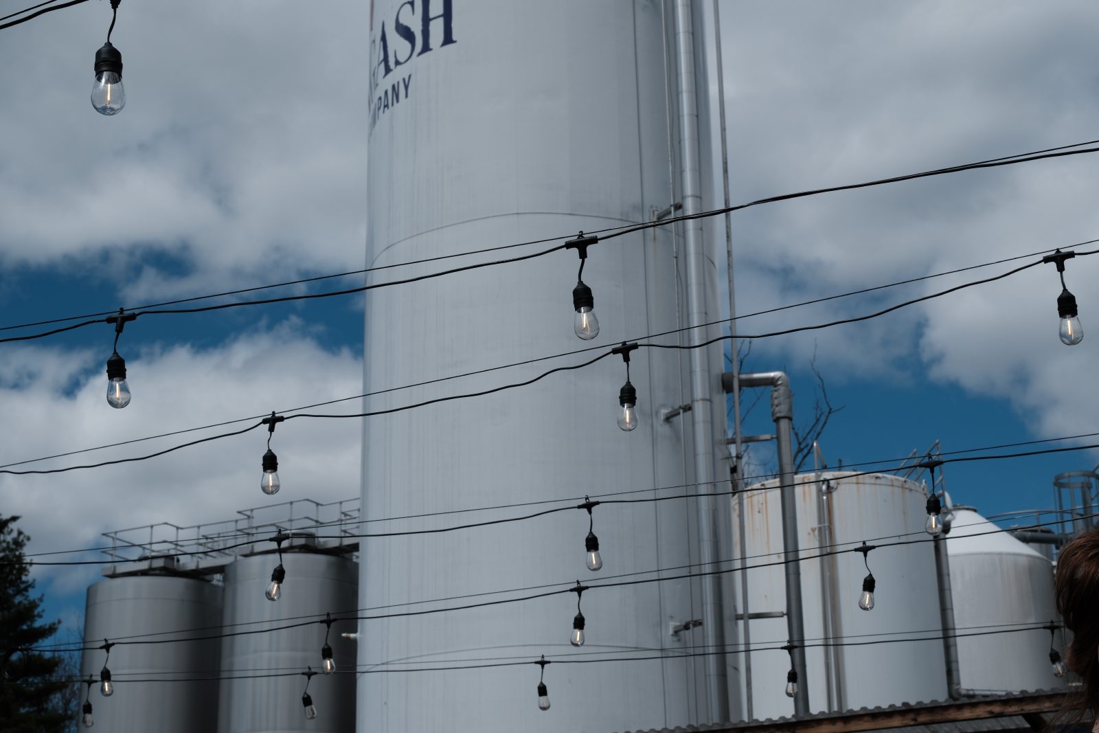 Stringed lights in the forefront of the brewing tanks outside Allagash